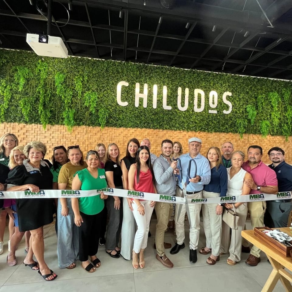 Restaurant ribbon-cutting ceremony with a group of people gathered beneath the illuminated CHILUDOS sign.