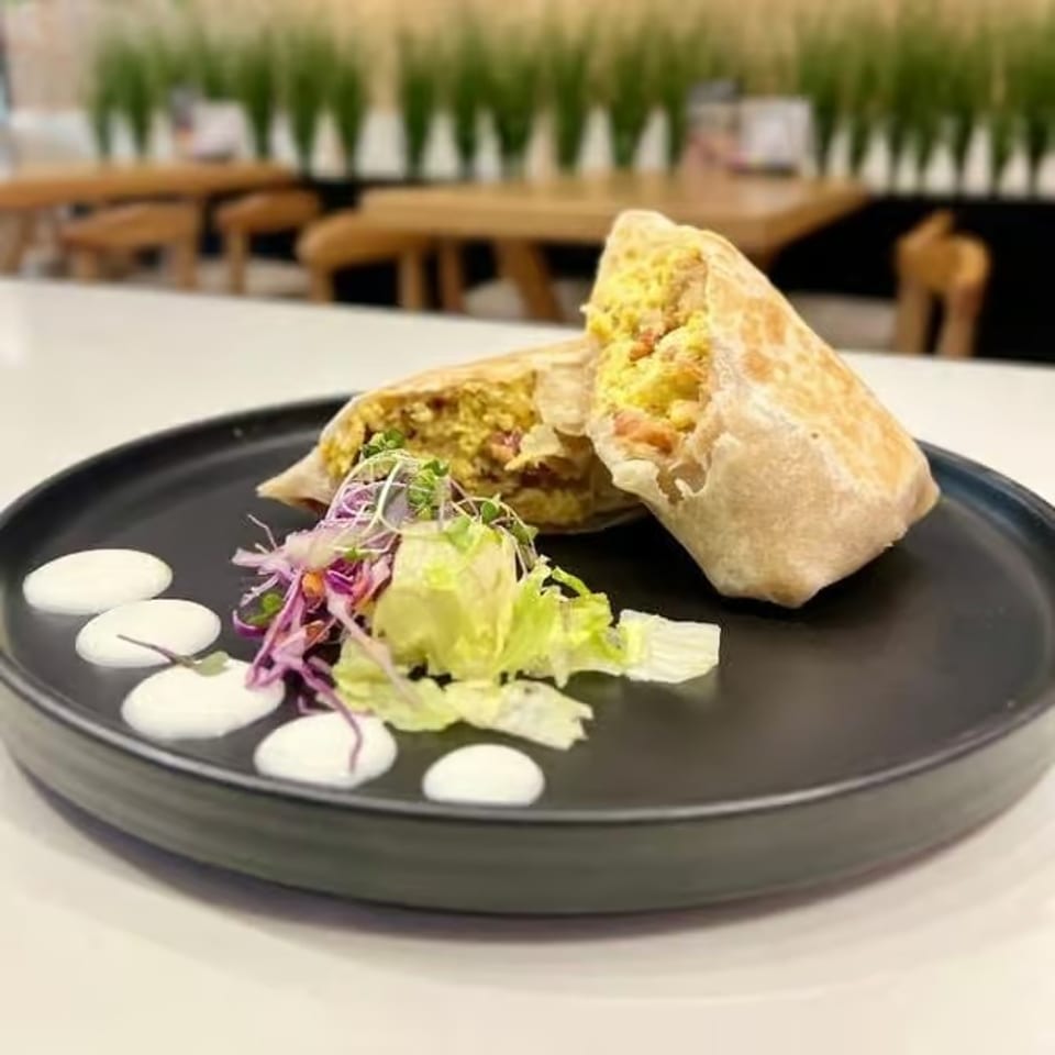 Two stuffed flatbread wraps with greens and white sauce dots on a black plate in a modern restaurant.